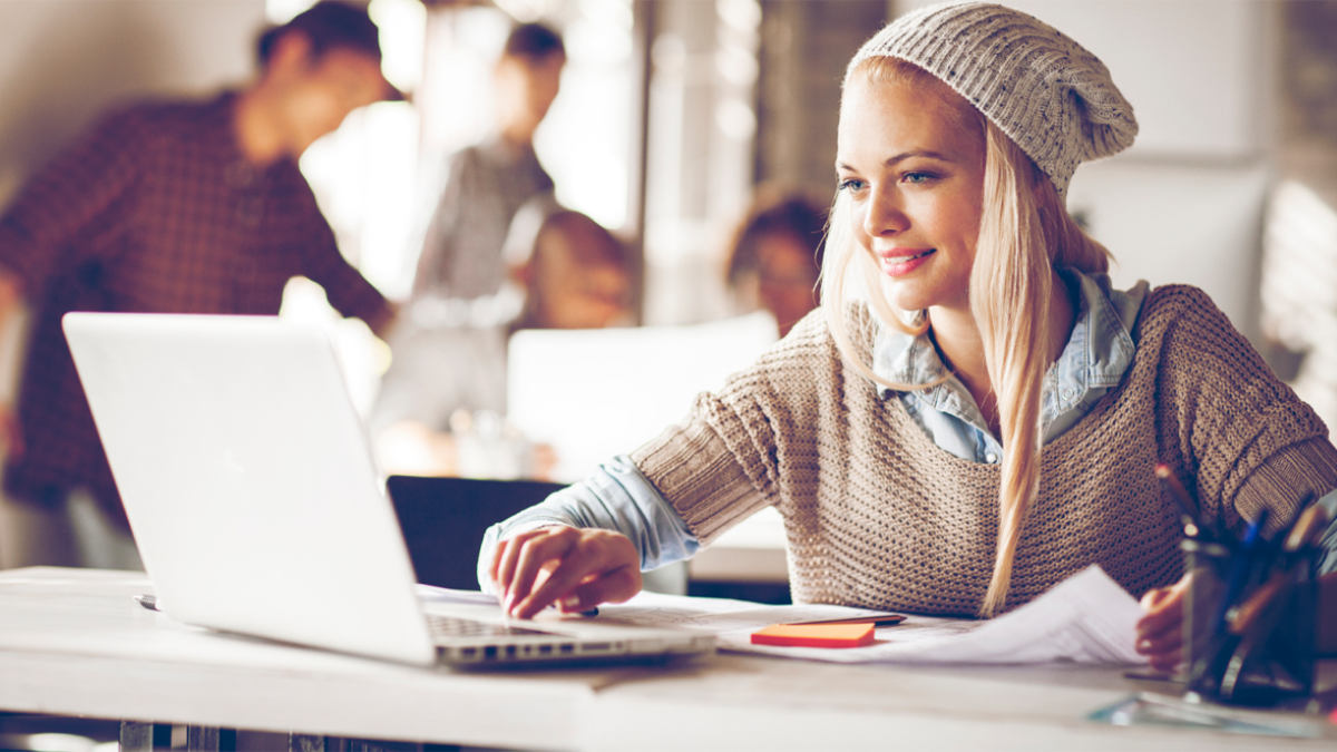 A woman smiling at her laptop while going over paperwork at a shared work table