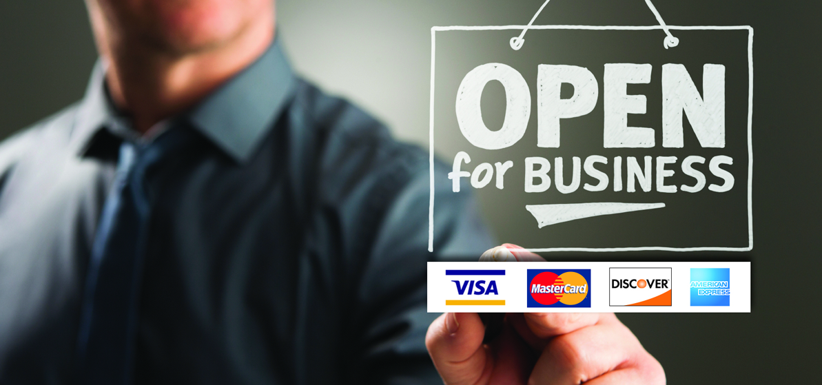 A man holding an Open for Business sign, with Visa, MasterCard, Discover and American Express logos