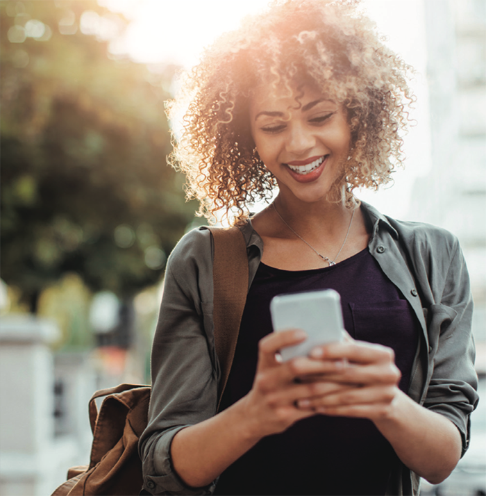 A woman smiling as she uses her phone on a city street