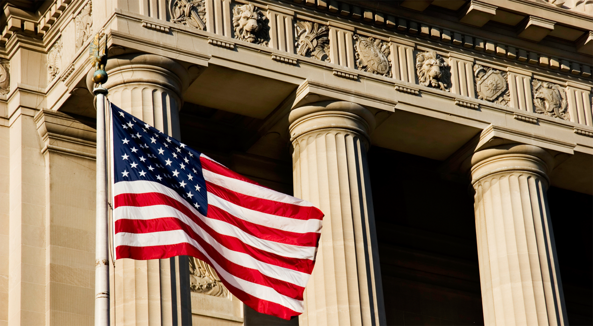 An American flag flying in front of the stone columns of a federal building